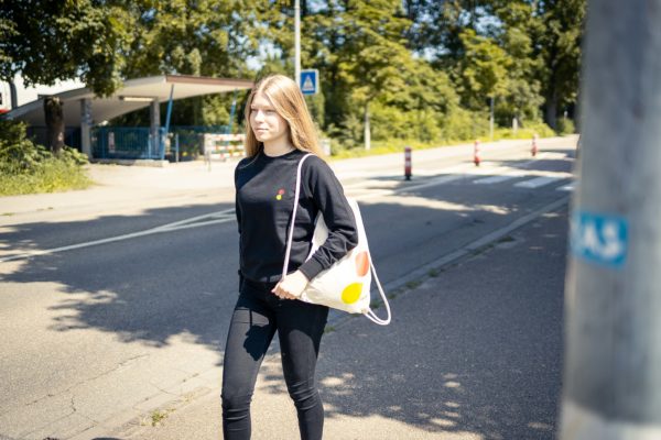 junge Frau mit Sportbeutel über der Schulter an einer Straße