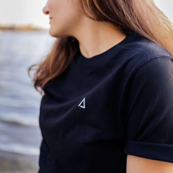 Weibliches Model trägt schwarzes Unisex T-Shirt mit weißem Karlmotte Dreieck