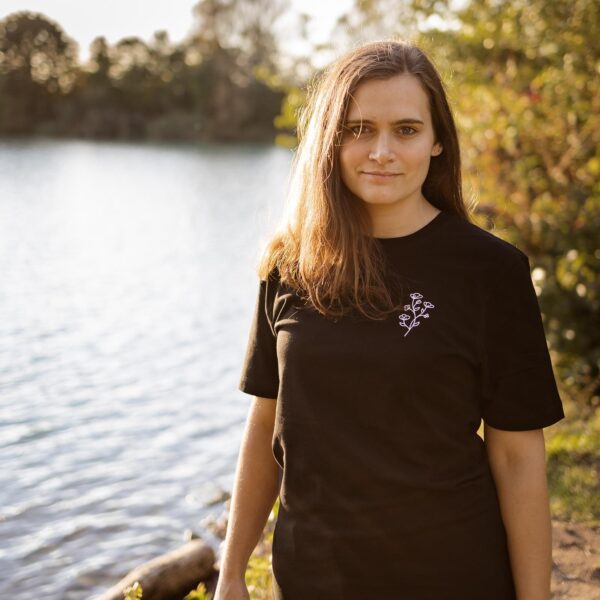 Weibliches Model trägt schwarzes Unisex T-Shirt mit weißem Blumenmotiv