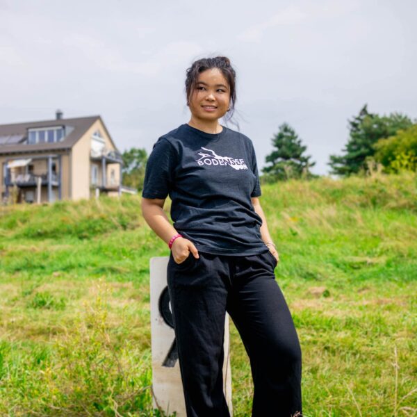 Weibliches Model trägt schwarz meliertes Unisex T-Shirt mit weißer Bodensee Karte