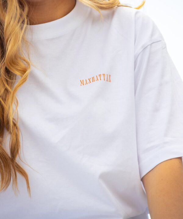 Nahaufnahme weißes Box Tee Shirt mit orangenen MANHATTAN Wortzug